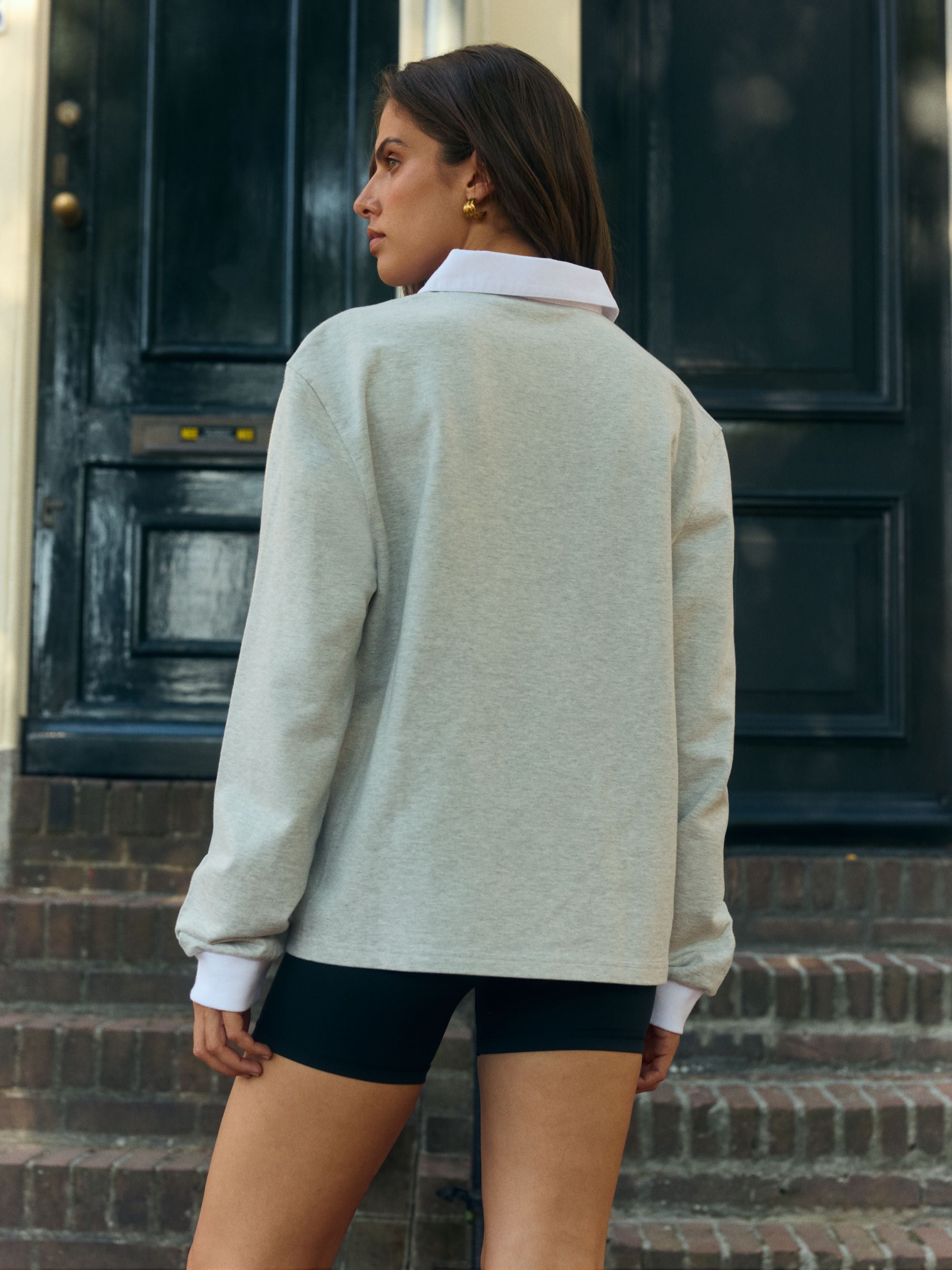 Woman wearing a grey CASPARA rugby shirt with a white collar seen from behind outdoors.
